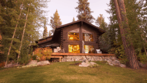 Charming wooden Brian Head rental cabin surrounded by pine trees with warm interior lights at sunset